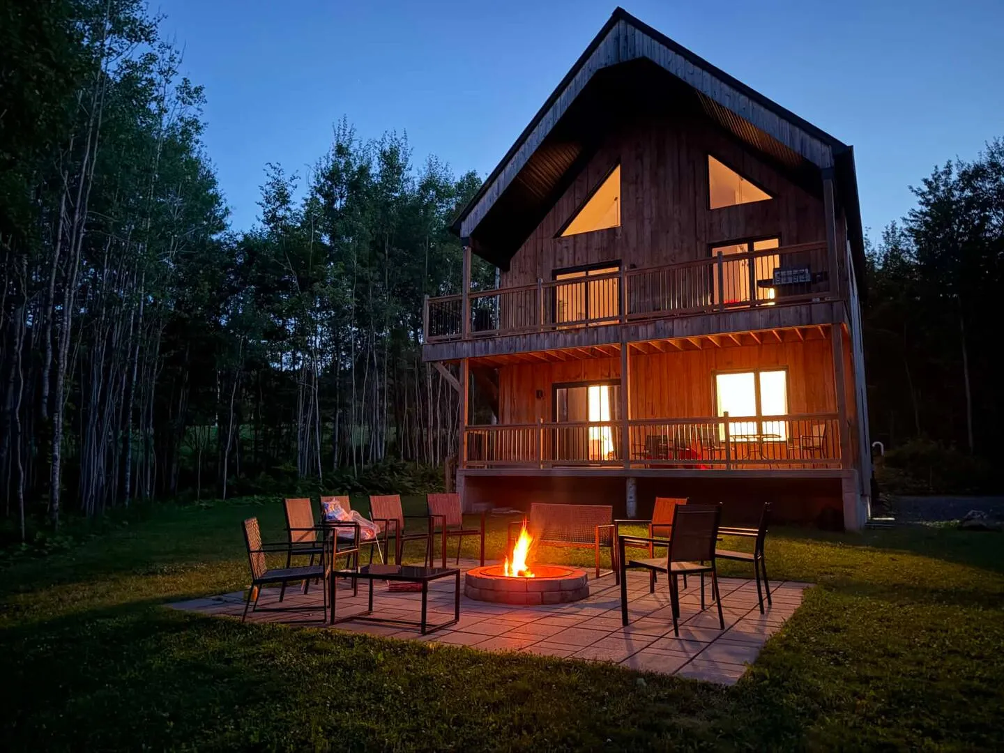 Villa Foresta in Coaticook at dusk, windows glowing, a fire lit on the patio
